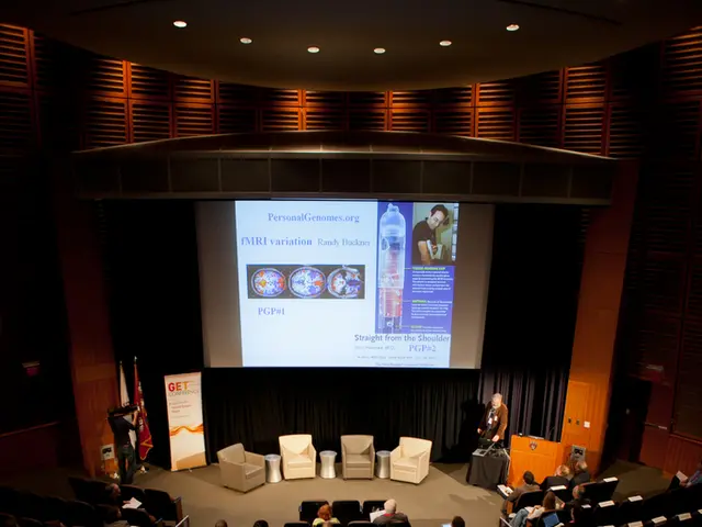 In this image we can see an auditorium. There are many people sitting on the chairs and holding...