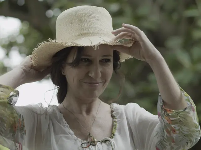 In this image I can see a woman is adjusting her hat. She wore white color dress, she is smiling.